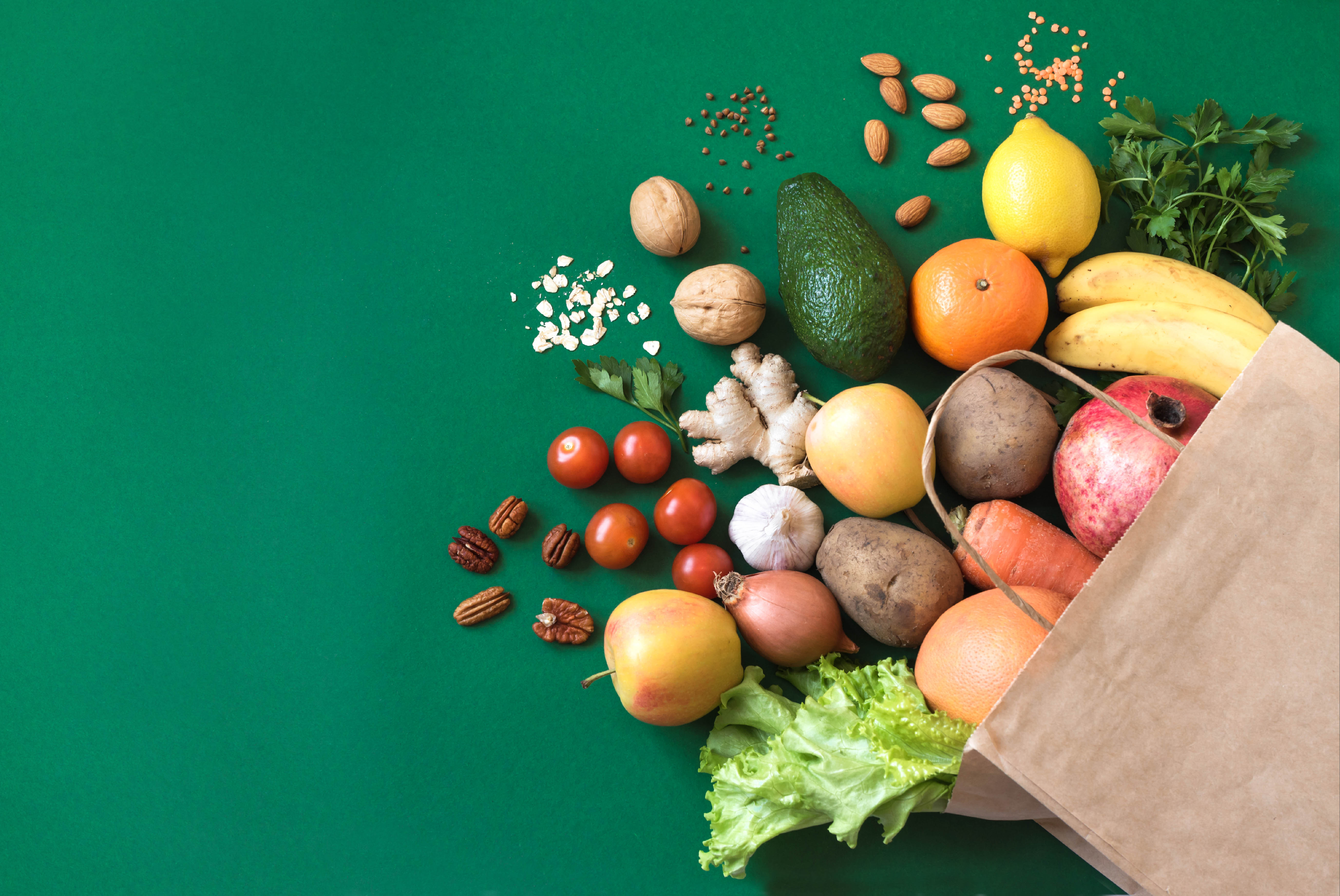 Bag of healthy groceries spilling out of paper bag on a forest green background Bag of healthy groceries spilling out of paper bag on a forest green background